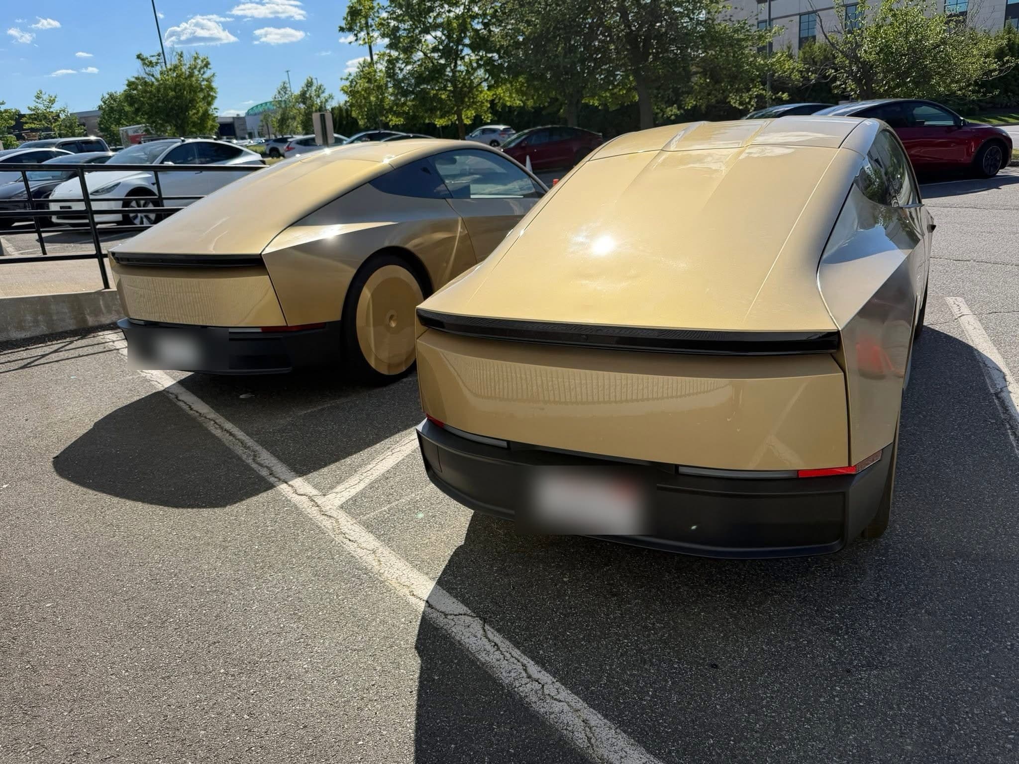 Two gold-camo Tesla Cybercab test units parked at Tesla Peabody, license plates obscured